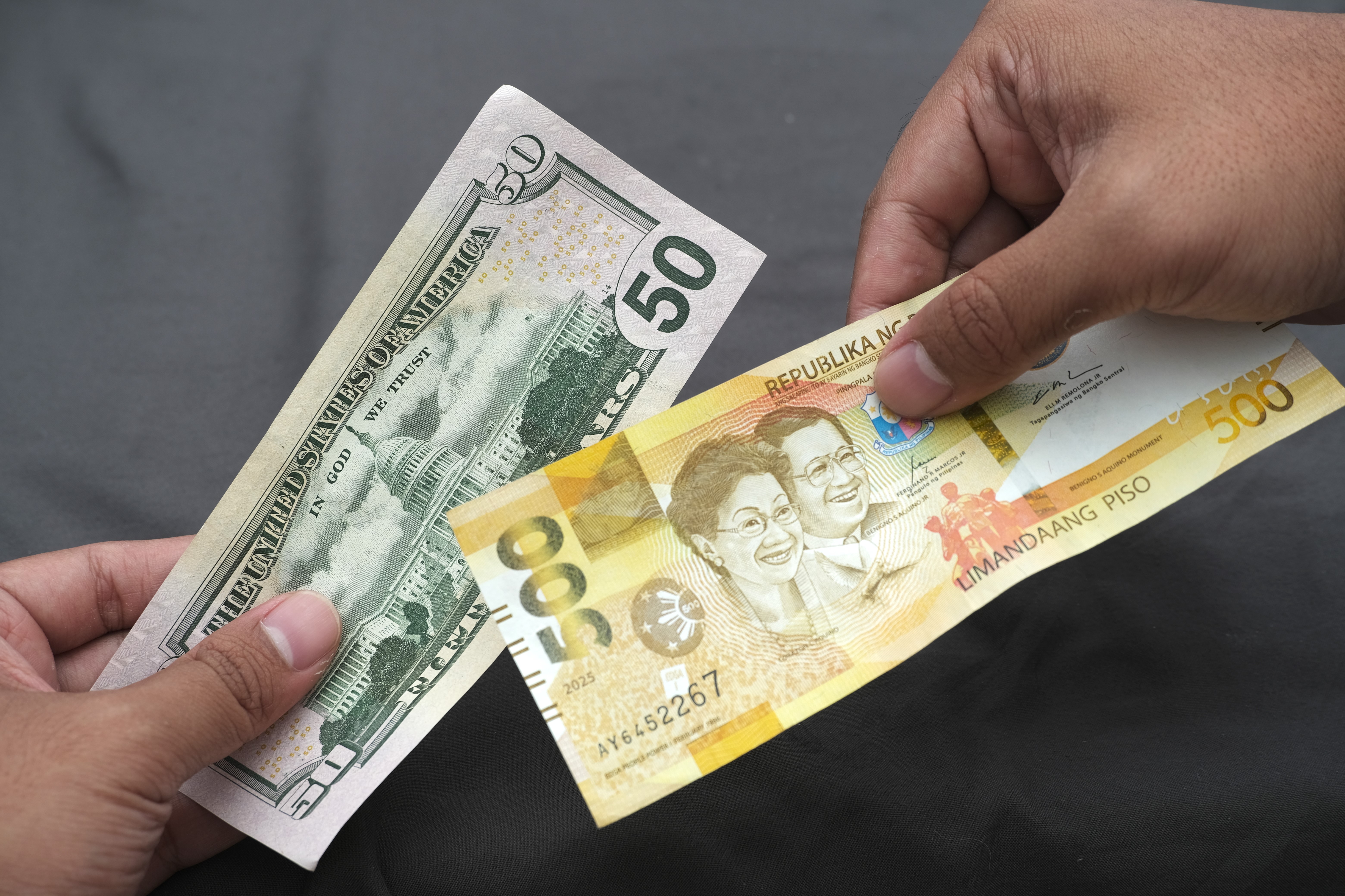 Close-up of hands holding Philippine peso and US dollar banknotes, showing currency exchange, travel finance, and money comparison.